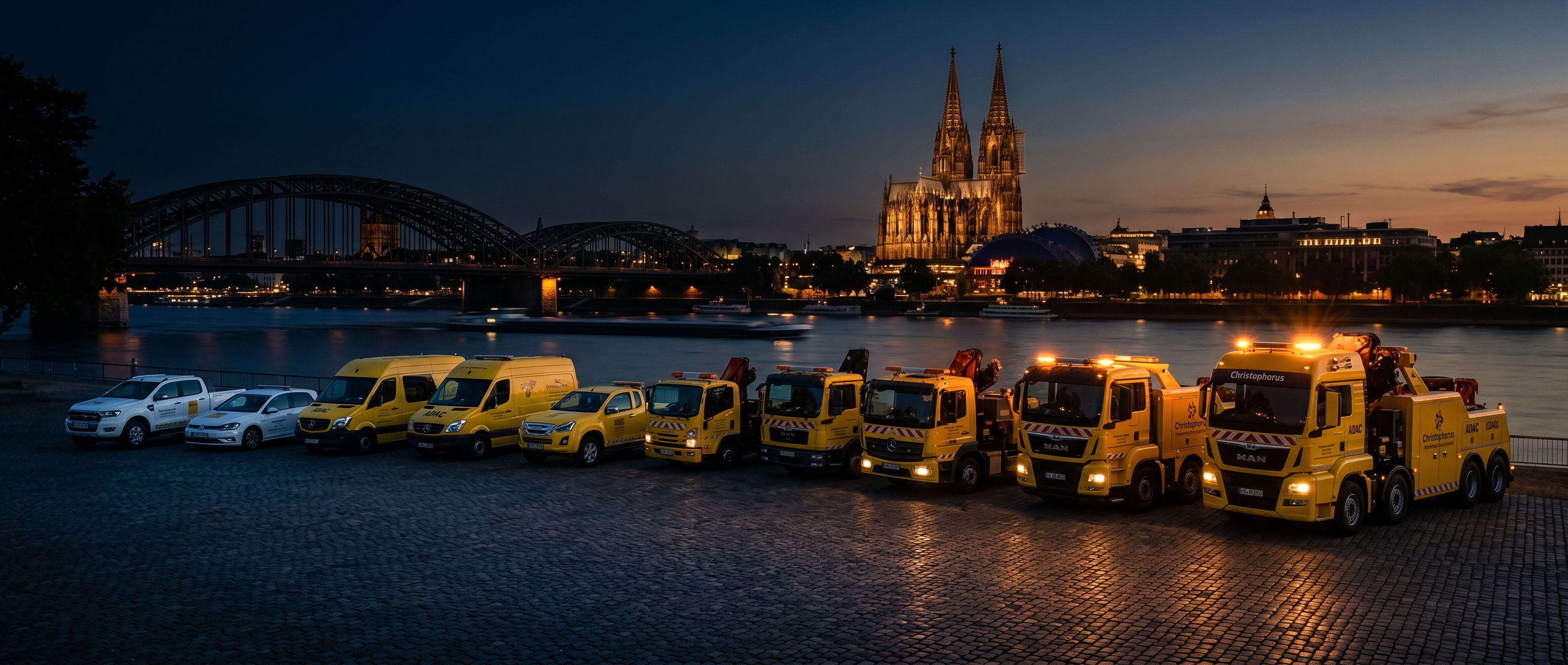 Christophorus Pannenservice Flotte am Kölner Rheinufer mit beleuchtetem Dom und Hohenzollernbrücke bei Nacht